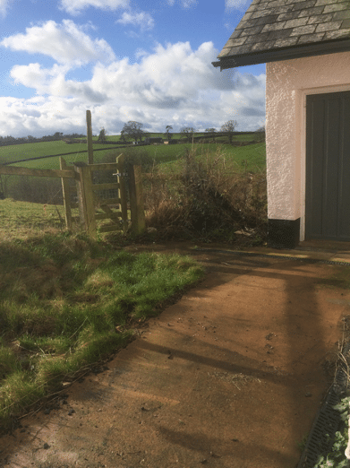 rough looking garden with concrete driveway and fields in background