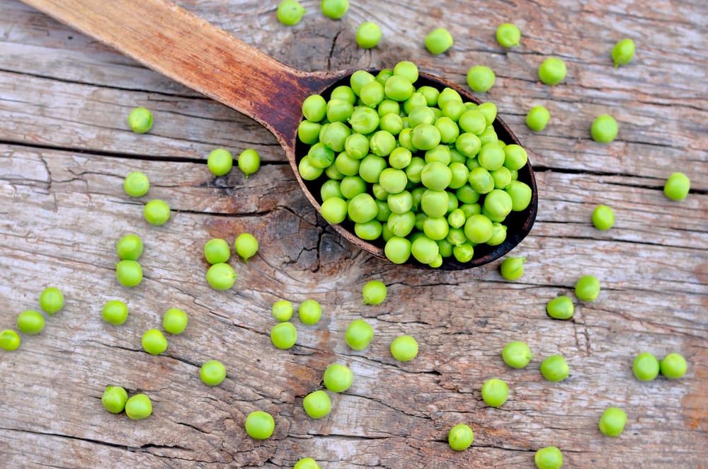 Green peas sat on a wooden spoon